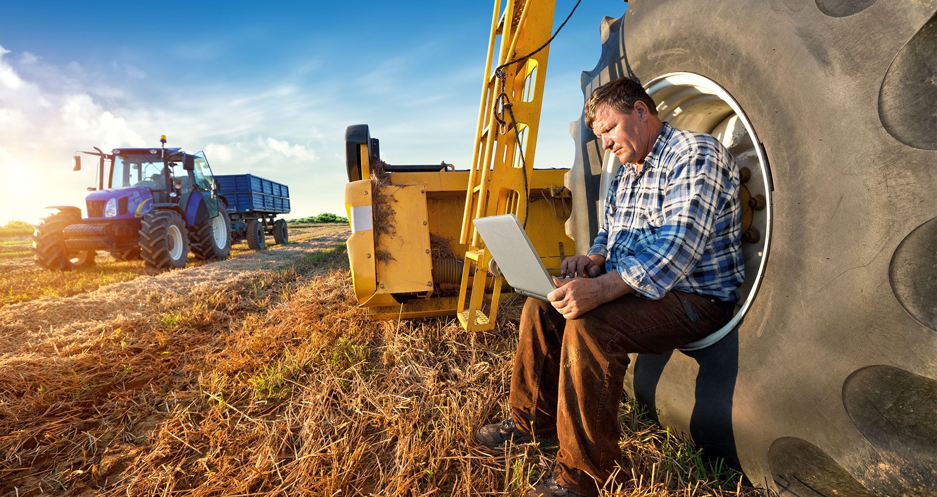 A man sitting inside a massive vehicle wheel, using his laptop, in a rural area