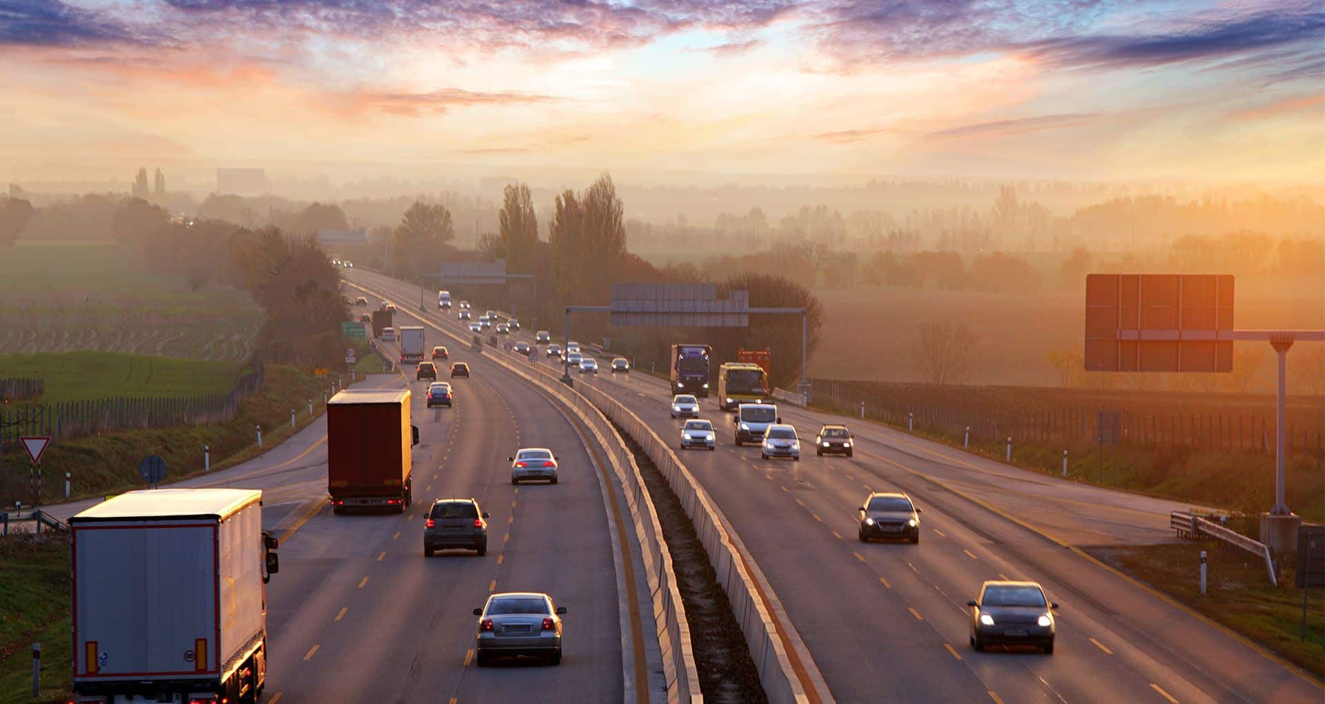 A number of cars and trucks driving down the freeway at sunset